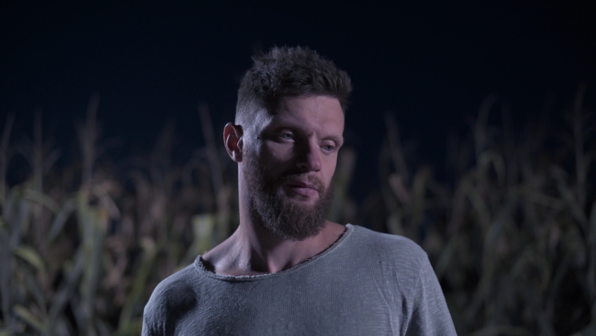 Scary man with ax stands in corn field and looks into camera at night. Close-up portrait. Halloween concept