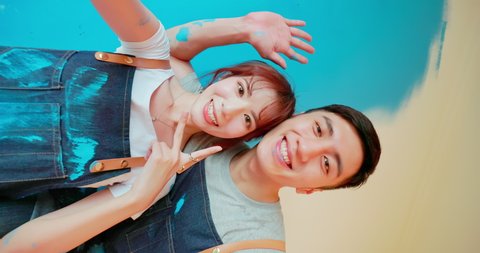 vertical video of young asian couple decorate home - they take selfie by mobile phone after painting wall with blue color