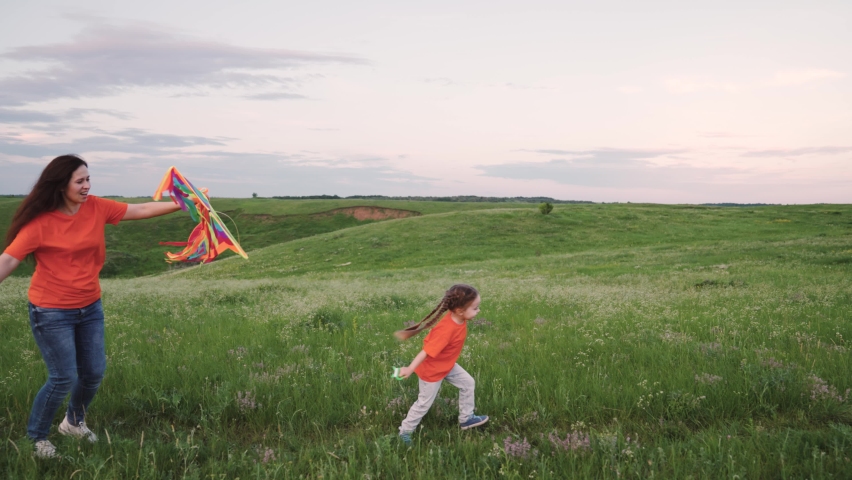 Daughter and mother launch kite into sky, the baby runs through green grass with a kite in his hand. child, girl playing in park with her family. Children