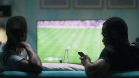 African American man using smartphone and clinking bottles of beer with friends while chilling on sofa and watching soccer game on TV - Powered by Shutterstock - Get 15% off with code: PIKWIZARD15