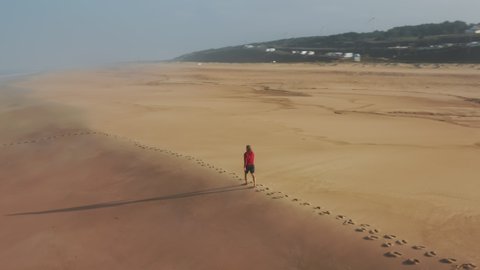 Aerial view of idyllic landscape with the Atlantic Ocean. Man strolling along the shoreline within perfect summer destination as seen from the top. High quality 4k footage