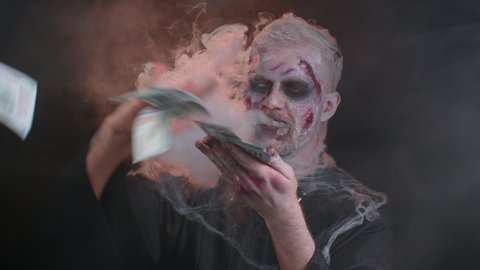 Portrait of sinister man in carnival costume of Halloween zombie with bloody wounded scars face throwing money dollar cash banknotes. Horror theme of cosplay wounded undead, beast, monster