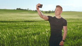 A young man is standing in a field and recording video on the front camera of his phone. He is talking while looking at the camera. He's wearing a sports uniform. 4K 50fps
