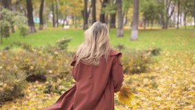 Young beautiful wonam on a walk in autumn park, runs and throws leaves. Outdoor shot of a happy young model running along the path. Tinted image. High quality FullHD video. High quality FullHD footage