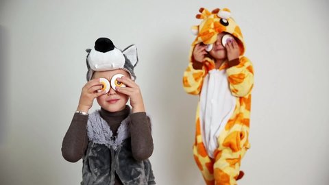 Funny boy in a wolf costume and a girl in a giraffe costume playing with eye-looking cookies. Studio shot