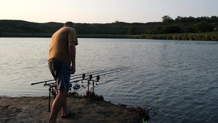 Fisherman pulls the fish out of the river with carp fishing equipment. Angler with carpfishing rod in a beautiful summer sunset during a bite.