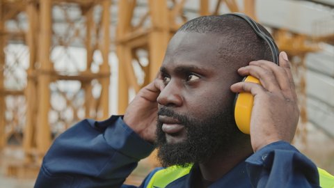 Close up of African-American construction worker putting on noise-cancelling earmuffs