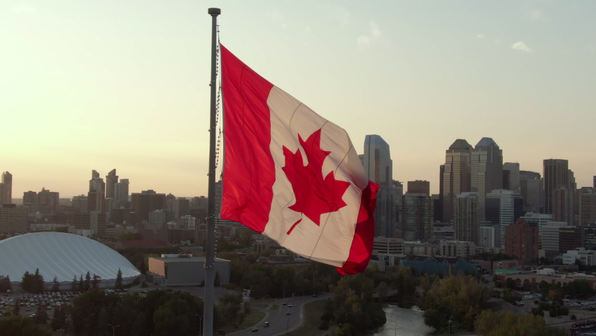 Aerial orbiting shot showing Canadian flag waving in the wind against the sun on Canada Day in Calgary, Alberta, Canada, North America. Royalty-Free Stock Footage #1079960720