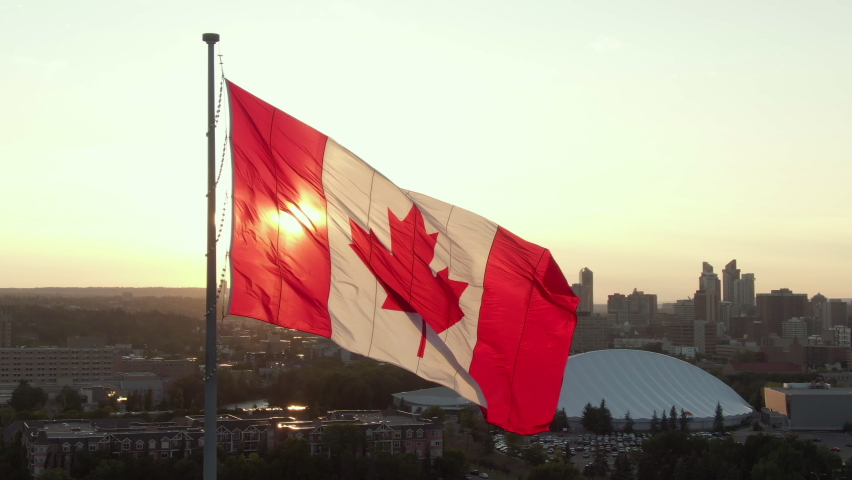 Aerial orbiting shot showing Canadian flag waving in the wind against the sun on Canada Day in Calgary, Alberta, Canada, North America. Royalty-Free Stock Footage #1079960720