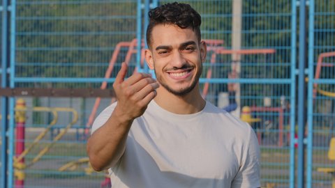 Attractive Arab sportsman making welcome gesture inviting to join team promoting healthy lifestyle and sports. Handsome strong middle eastern indian male athlete, trainer looking at camera waving hand