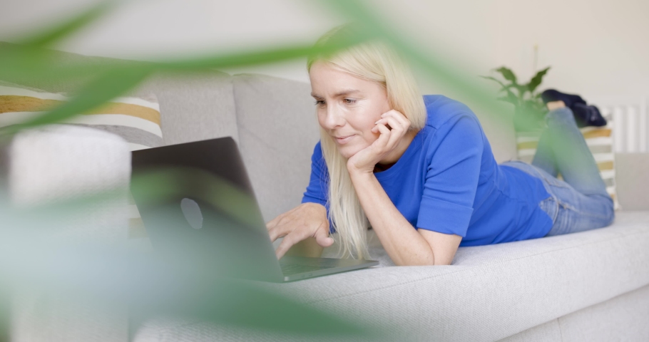 Young woman lying down on sofa using laptop