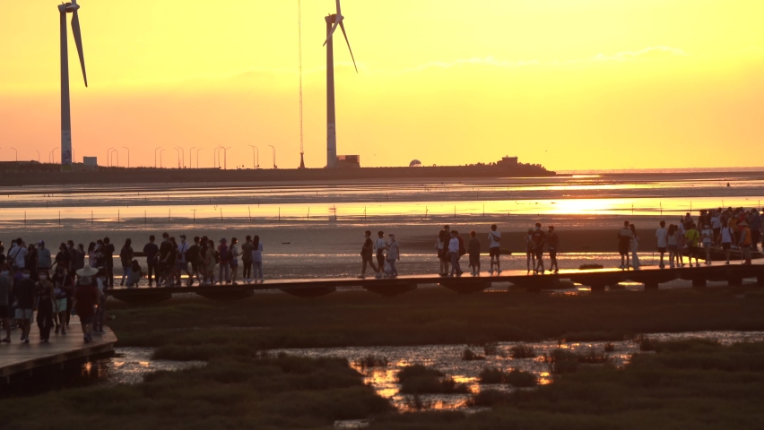 Beautiful orange sunset landscape shot overlooking at tourist crowds movement on the platform at pristine attraction Gaomei wetland preservation area, Taichung city, Taiwan.