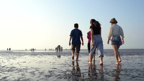 Tourists walking barefoot on muddy tidal flats, experiencing and enjoying the nature on tranquil afternoon with beautiful water reflection on the ground at Gaomei wetland preservation area, Taichung.