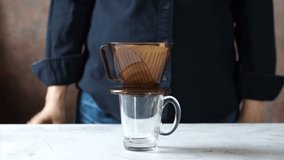 Video clip brewed drip coffee making, hand of barista pouring hot water onto ground coffee beans contained in paper filter, then allowing to brew. Aromatic hot drink preparation and brewing process.