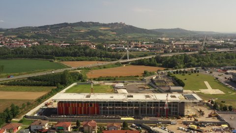 Big city under construction in a suburban zone of Piedmont, Italy. Residential houses, highway with a modern bridge, mountains, construction crane, heliport. Panoramic aerial drone view 4K.