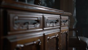 Closeup antique wooden chest of drawers in classical interior. Vintage dresser in dark room. Carved wood commode indoors. Close up wood furniture details. Design interior concept.