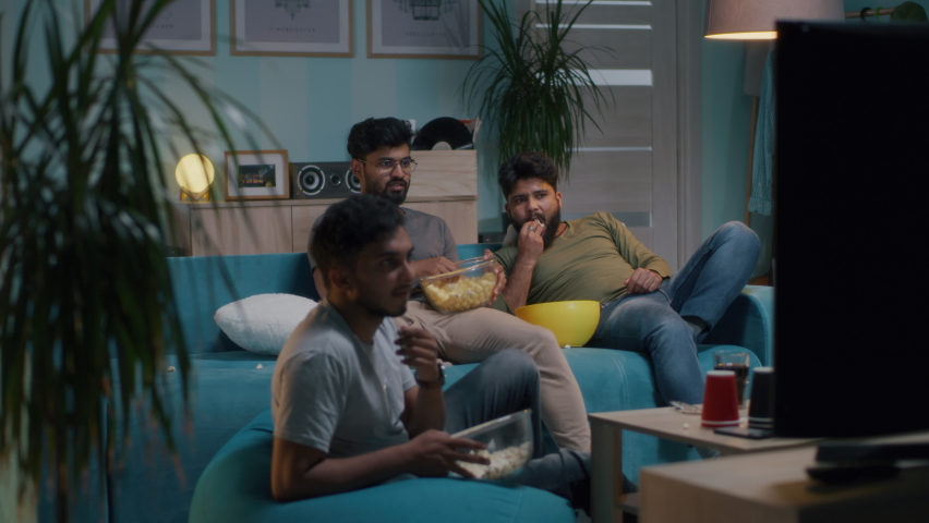 Indian men in casual clothes throwing popcorn and giving high five while watching sports match on TV in living room at home Royalty-Free Stock Footage #1080002837
