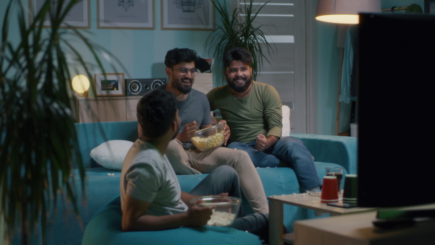 Indian men in casual clothes throwing popcorn and giving high five while watching sports match on TV in living room at home Royalty-Free Stock Footage #1080002837