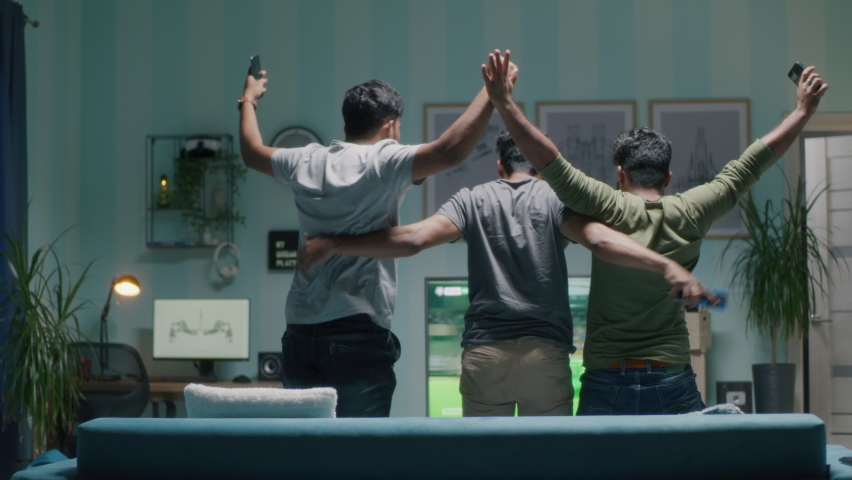 Back view of men with smartphones standing up from sofa and hugging each other while celebrating victory of favorite soccer team Royalty-Free Stock Footage #1080002840