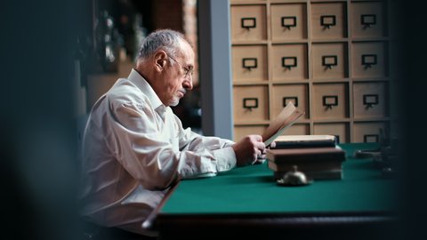 Focused 70s elderly man scientist writer author professor lawyer reading antique letters paper documents. Confident old male working at library book archive storage sitting at desk workplace side view