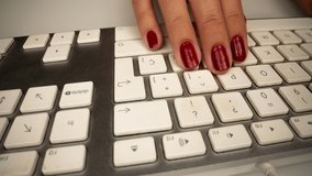 Panning across a computer keyboard with the hands of a woman with red painted nails types