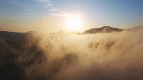 Drone flying through beautiful golden sunny cloudscape at sunrise 4K. Amazing aerial shot of heaven clouds in blue sky. Cinematic 4K of sun shining above clouds and mountains with beautiful lens flare