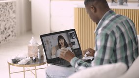 Online appointment and telemedicine. Male African American sick patient waving greeting his female gp doctor, communicating online using video call on laptop, while sitting on sofa at home