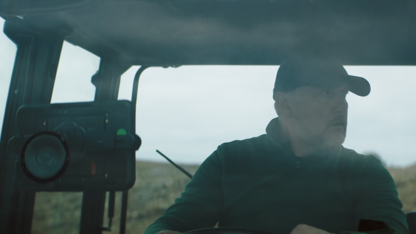 Portrait of 50s Caucasian male farmer driving a tractor through the field. Shot with 2x anamorphic lens Royalty-Free Stock Footage #1080014252