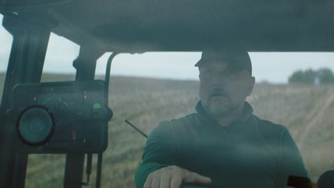 Portrait of 50s Caucasian male farmer driving a tractor through the field. Shot with 2x anamorphic lens