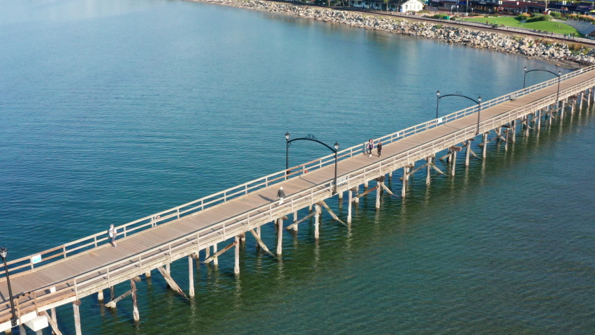 Aerial Drone of the White Rock Pier in British Columbia Canada. People Walking Across Attraction Surrounded By Pacific Ocean and Blue Water