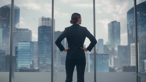 Successful Businesswoman in Stylish Suit Looking out of the Window at Big City in Downtown Area. Confident Female CEO Working on Financial Projects. Real Estate Agent Planning a Development Deal.
