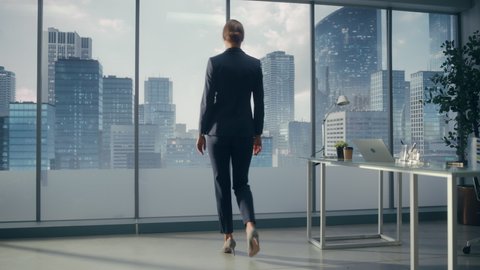 Successful Businesswoman in Stylish Suit Looking out of the Window at Big City in Downtown Area. Confident Female CEO Working on Investment Opportunity. Real Estate Agent Planning a Development Deal.