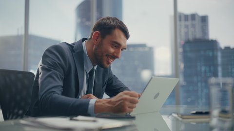 Excited Businessman in a Suit Sitting at a Desk in Modern Office, Using Laptop Computer. Successful Manager Ecstatic About Winning a Real Estate Investment Deal for Corporate Business.