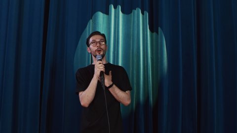 A young Caucasian comedian performing his stand-up monologue on the stage of a small venue. Stand-up concert