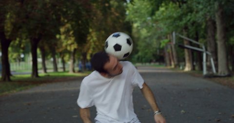 Cinematic shot of young carefree arab freestyle soccer player is juggling sport ball with his head and neck while training tricks of self-expression with football in public green park.