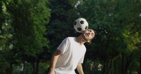 Cinematic shot of young carefree arab freestyle soccer player is juggling sport ball with his head and neck while training tricks of self-expression with football in public green park.