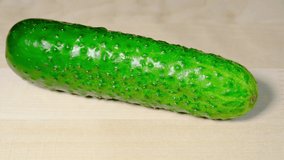 Slicing a cucumber with a large knife on a wooden chopping board close-up