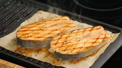 Red fish cut steak on cooking parchment paper. Salmon BBQ roasting on grids in restaurant. Flavored, seasoned and dressed with spices fish grill fries up. Appetizing marinated salmon chops barbeque.