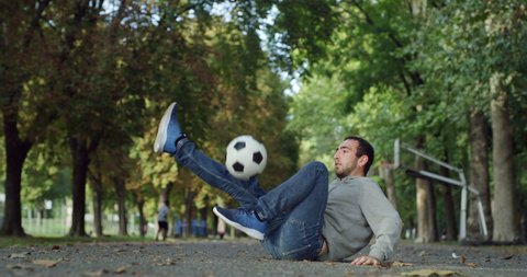 Cinematic shot of young carefree arab freestyle soccer player is juggling sport ball with his knee and feet while training tricks of self-expression with football in public green park.