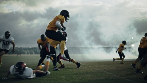 American Football Field Two Teams Play: Successful Player Jumping Over Defense Running to Score Touchdown Points. Professional Athletes Compete for the Ball, Fight for Victory. Dramatic Slow Motion