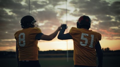 American Football Game Start Teams Ready: Two Professional Players Walk on Field Determined to Win the Match. Competitive Friends do Celebration High-Five. Immersive Handheld Following Shot