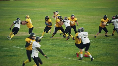 American Football Teams Start Game: Professional Players, Aggressive Face-off, Tackle, Pass, Fight for Ball and Score. Warrior Competition Full of Brutal Energy, Power, Skill. Slow Motion Wide Shot
