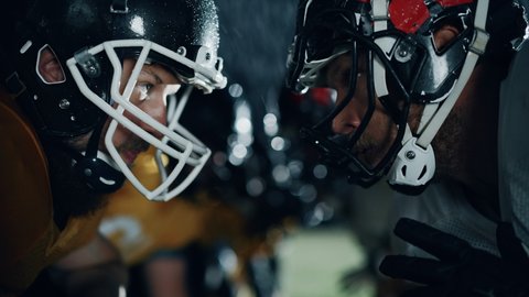 American Football Game Start Teams Ready: Close-up Portrait of Two Professional Players, Aggressive Face-off. Competition Full of Brutal Energy, Power, Skill. Cinematic Rainy Night. Dramatic Light