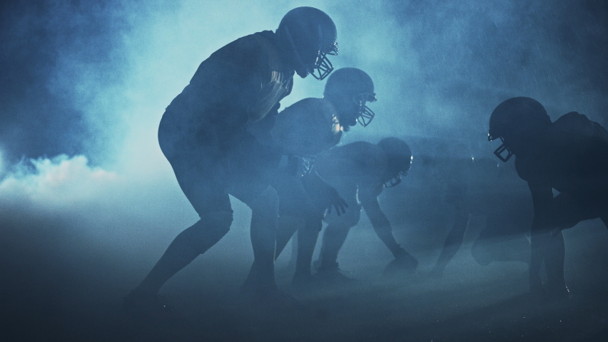 American Football Field Two Teams Compete: Players Pass, Run, Attack to Score Touchdown Points. Noisy Cinematic Shot. Rainy Night with Athletes Fight for the Ball in Dramatic Smoke. Slow Motion Royalty-Free Stock Footage #1080022376