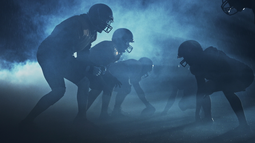 American Football Field Two Teams Compete: Players Pass, Run, Attack to Score Touchdown Points. Noisy Cinematic Shot. Rainy Night with Athletes Fight for the Ball in Dramatic Smoke. Slow Motion | Shutterstock HD Video #1080022376