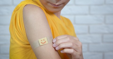 Time for covid vaccination. A child show her band-aid with smiling emoticon on hand after vaccination. A concept of world immunization time.