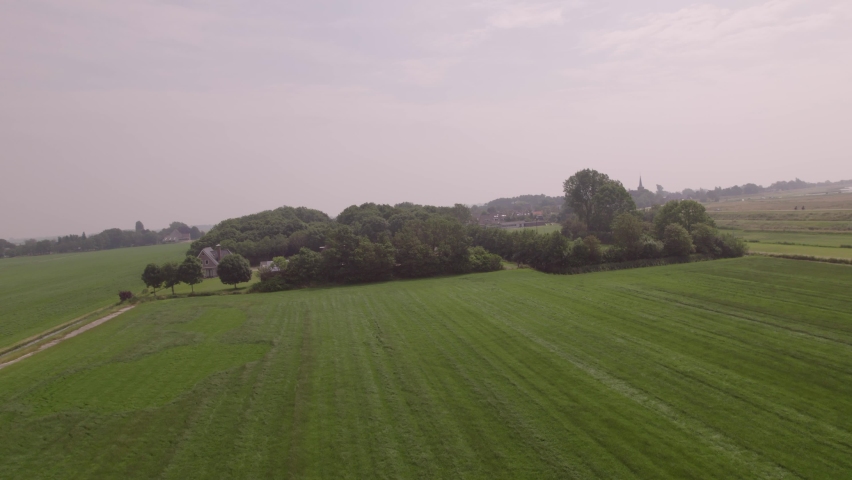 Drone aerial view B-Roll: Bird's eye view over the fields and a park, in the background a lake. On the dike a passing car, cyclists and in the field a rotating windmill and a stationary windmill. Royalty-Free Stock Footage #1080024974