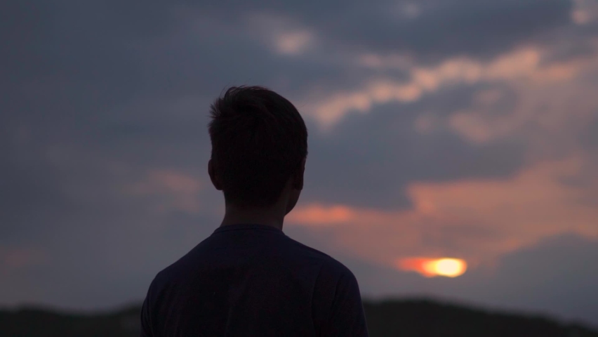 Silhouette of an Indian kid looking at the orange sky during the sunset. Hopeful kid stares at the sun. Kid lost in deep thoughts after looking at the sunset.  Royalty-Free Stock Footage #1080025601