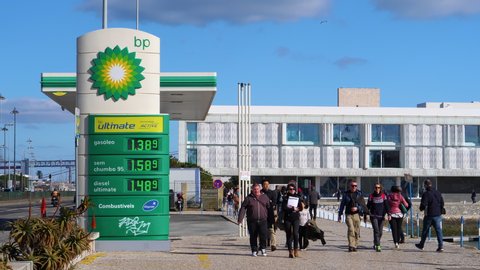 LISBON, PORTUGAL - FEB 10, 2018: People pedestrians walking in front of modern BP British Petroleum gas station with green element on paved concrete street in sunlight near harbour