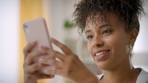 Portrait of Happy Business African American Woman Using Mobile Phone at Home Office or Living Room. Happy Millennial Authentic Real Girl Close up.